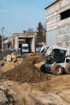 White skid steer loader at a construction site working with a soil. Industrial machinery. Industry