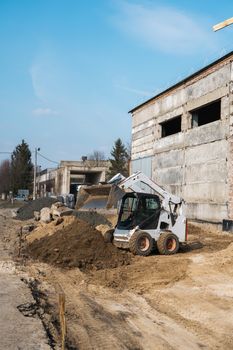 White skid steer loader at a construction site working with a soil. Industrial machinery. Industry