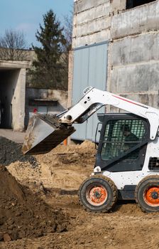 White skid steer loader at a construction site working with a soil. Industrial machinery. Industry