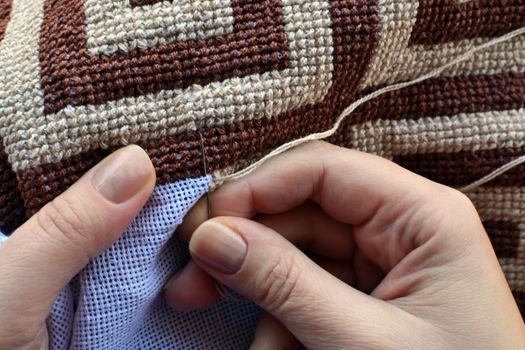 Hands of woman embroidering traditional pattern with geometric motifs