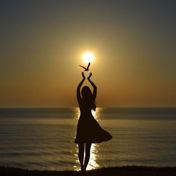 Freedom concept with silhouette of bird flying out of woman hands on the sea shore