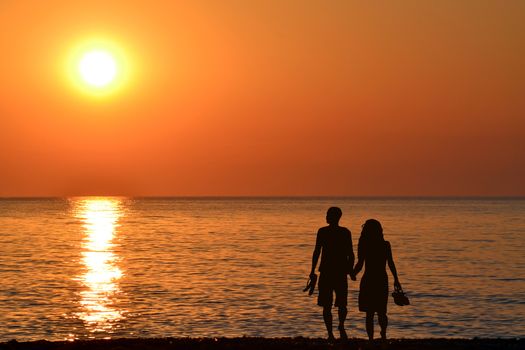 Back view of a couple silhouette walking together on the beach at sunrise in summer