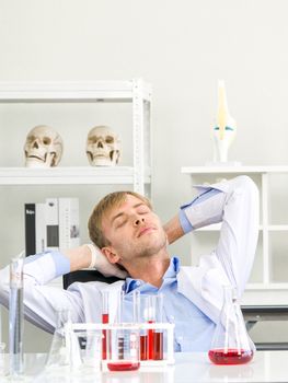 A young Brazilian scientist rested his eyes and neck after completing his research. Working atmosphere in chemical laboratory. Test tubes filled with chemicals on the table.