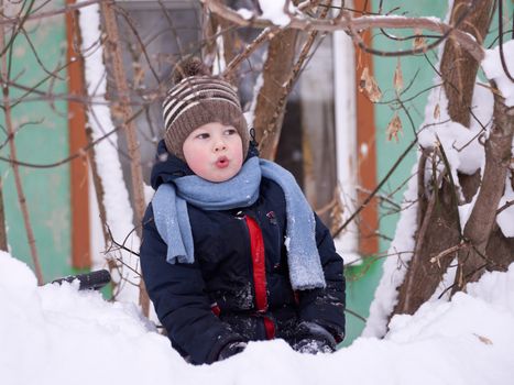 A boy in a knitted hat and with a knitted scarf in winter plays in the snow.