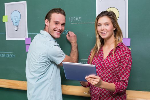 Portrait of young creative business people with digital tablet by blackboard