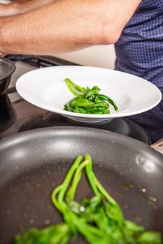 hands of cook preparing food in a frying pan with meat and vegetables