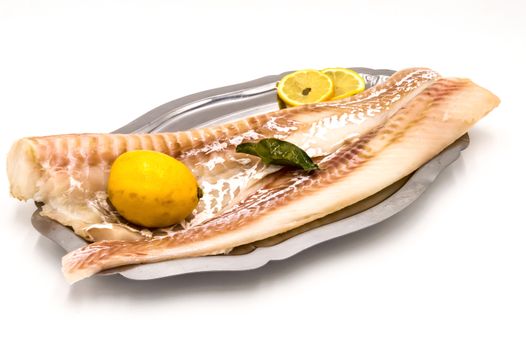 Cod fillets on a stainless steel dish with a lemon on a white background