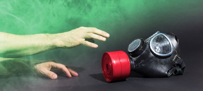 Man in room filled with smoke, trying to reach for vintage gasmask - Isolated on black - Green smoke