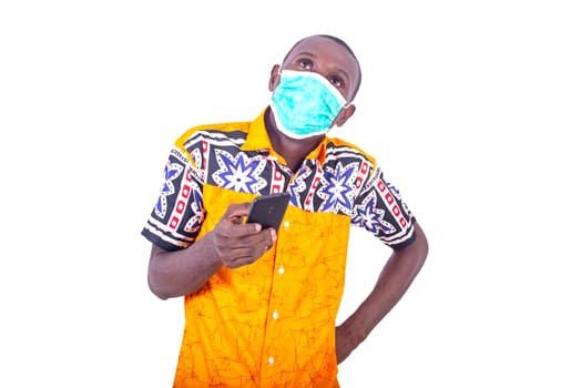 handsome young man wearing medical mask, holding cellphone while keeping hands on hips.