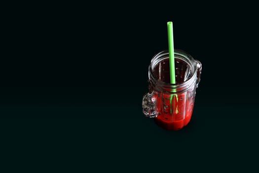 glass of tomato juice in with a green straw with a black background