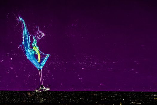 New Years concept of a crashing alcohol glass with purple background and blue fluids