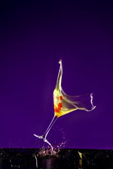 New Years concept of a crashing alcohol glass with purple background and yellow fluids