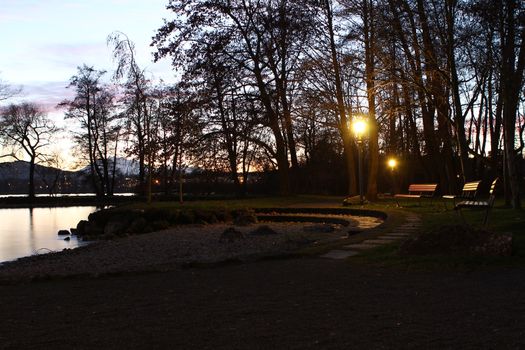 twilight by the lake in Cham, Zug with the swiss alps, with sun glowing through trees