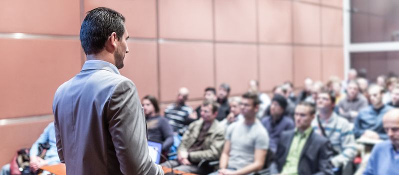 Speaker giving a talk on corporate business conference. Unrecognizable people in audience at conference hall. Business and Entrepreneurship event.