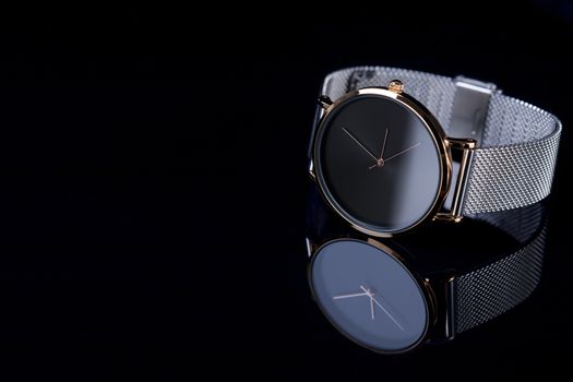 Black wrist watch for women with metal bracelet on glossy black background.