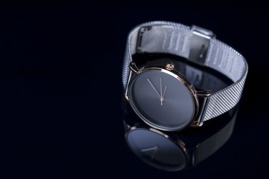 Black wrist watch for women with metal bracelet on glossy black background. Focus on the key of the watch