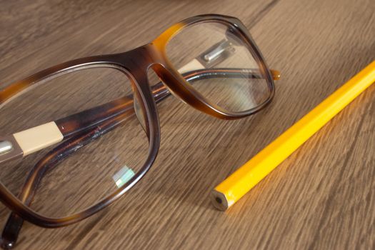 Par of glasses and a pencil on top of a wooden table