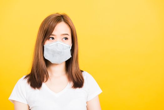 Asian happy portrait beautiful cute young woman standing wear t-shirt making mask protection from virus epidemic or air pollution looking side isolated, studio shot yellow background with copy space