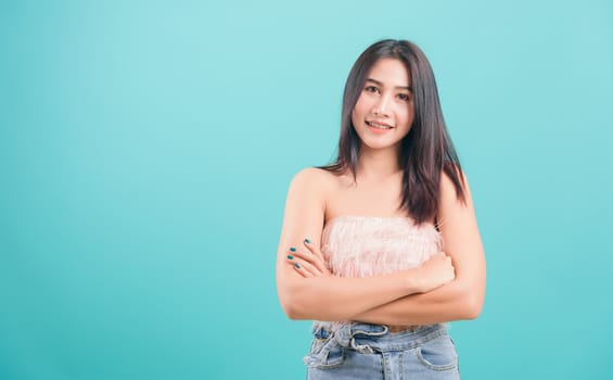 Asian happy portrait beautiful young woman standing smiling white teeth her keeping arms crossed and looking to camera on blue background with copy space for text