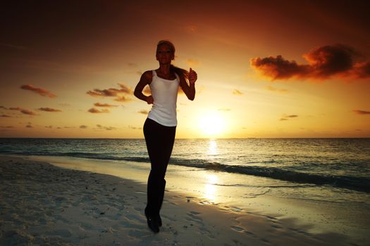 Woman run along the sea coast of sunrise or sunset behind