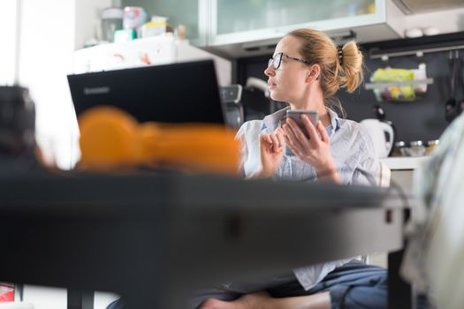 Stay at home and social distancing. Woman in her casual home clothing working remotly from kitchen dining table. Video chatting using social media with friend, family, business clients or partners.