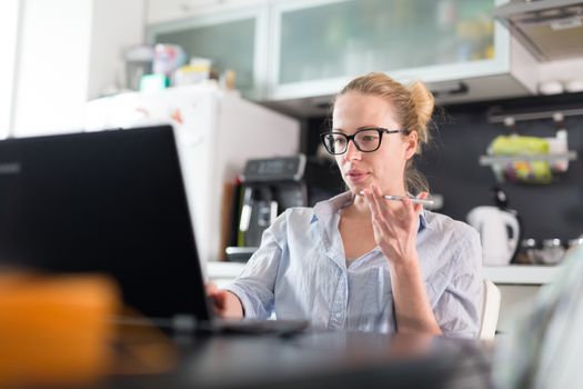 Stay at home and social distancing. Woman in her casual home clothing working remotly from kitchen dining table. Video chatting using social media with friend, family, business clients or partners.