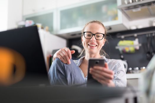 Stay at home and social distancing. Woman in her casual home clothing working remotly from kitchen dining table. Video chatting using social media with friend, family, business clients or partners.