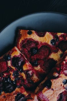 Berry pie on black plate, rustic homemade food with organic ingredients on black background