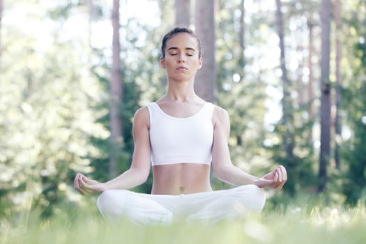 Young woman in white sportswear doing yoga lotus exercise outdoors