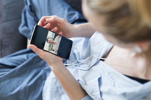 Stay at home, social distancing lifestyle. Woman at home relaxing on sofa couch using social media on phone for video chatting with her loved ones during corona virus pandemic.