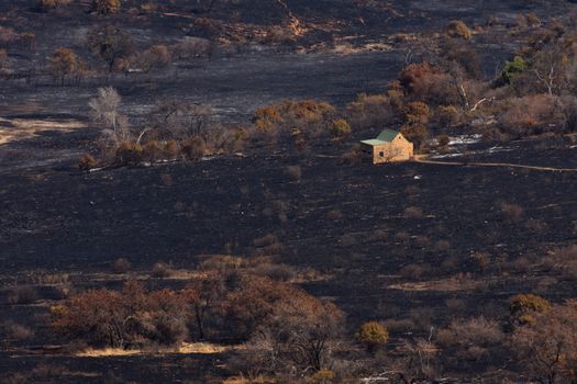 Burnt countryside farm terrain with small stone house building, Rustenburg, South Africa