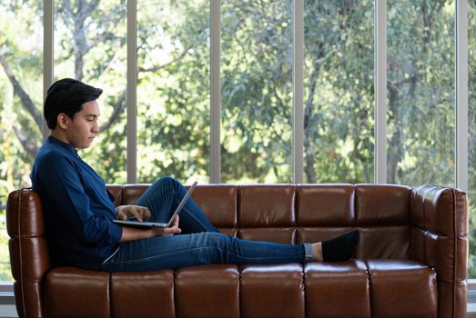 Asian man spend holidays in the living room. The young man wore comfortable clothes use laptop computer to search for jobs.