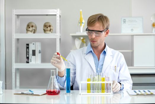 A young Brazilian scientist with a safety glasses lab is mixing cosmetic chemicals together carefully. Working atmosphere in chemical laboratory. Test tubes filled with chemicals on the table.