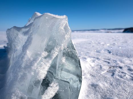 The icy beauty of ice cube, unusual shapes. Closeup crystal clear ice cube that covered with white snow. Lake Baikal, Russia