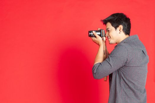 Young Asian hipster man searching for an interesting subject on the studio on a red background.Travel Lifestyle concept