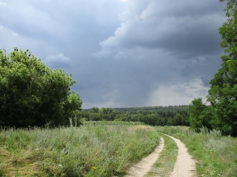 Photo of the country road in a field during a thunderstorm, summer