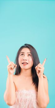 Smiling face Asian beautiful woman her point finger up on blue background, with copy space for text