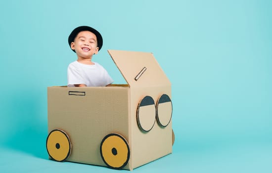 Happy Asian children boy smile in driving play car creative by a cardboard box imagination, summer holiday travel concept, studio shot on blue background with copy space for text