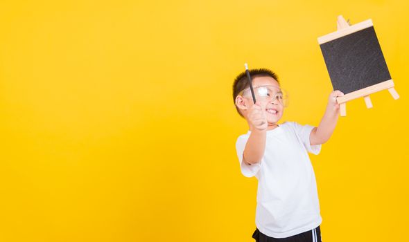 Asian Thai happy portrait cute little cheerful child boy smile he showing blackboard and looking to camera, studio shot isolated on yellow background with copy space