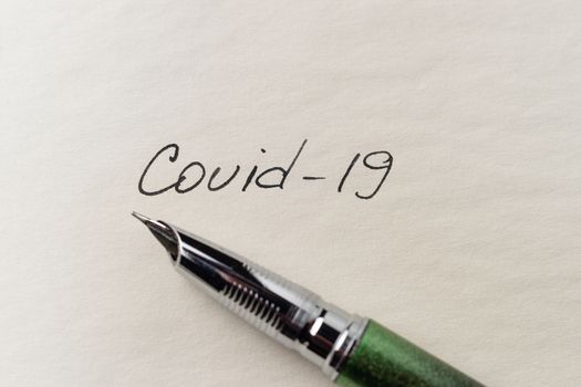 Covid-19 inscription on a blank empty sheet of paper in a notebook. Nearby lies a fountain pen. A lot of space for inscriptions and copyspace. The virus is dangerous. Blank for inscriptions. Template for article or cover.