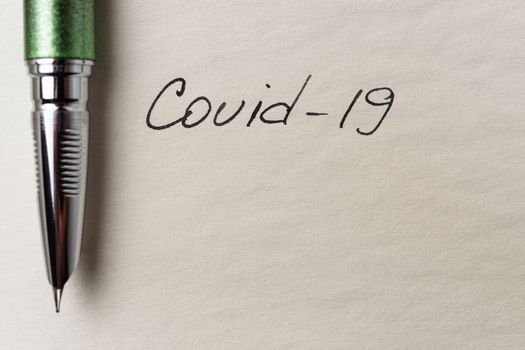 Covid-19 inscription on a blank empty sheet of paper in a notebook. Nearby lies a fountain pen. A lot of space for inscriptions and copyspace. The virus is dangerous. Blank for inscriptions. Template for article or cover.