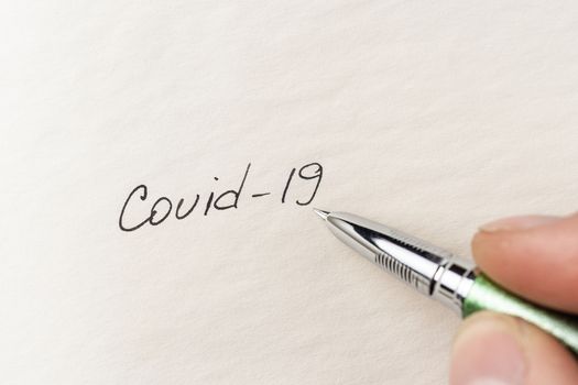 The hand writing Covid-19 on empty sheet of paper. Covid-19 inscription on a blank empty sheet of paper in a notebook. Nearby lies a fountain pen. A lot of space for inscriptions and copyspace. The virus is dangerous. Blank for inscriptions. Template for article or cover.