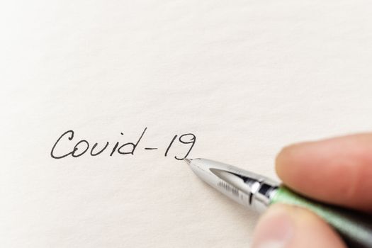 The hand writing Covid-19 on empty sheet of paper. Covid-19 inscription on a blank empty sheet of paper in a notebook. Nearby lies a fountain pen. A lot of space for inscriptions and copyspace. The virus is dangerous. Blank for inscriptions. Template for article or cover.