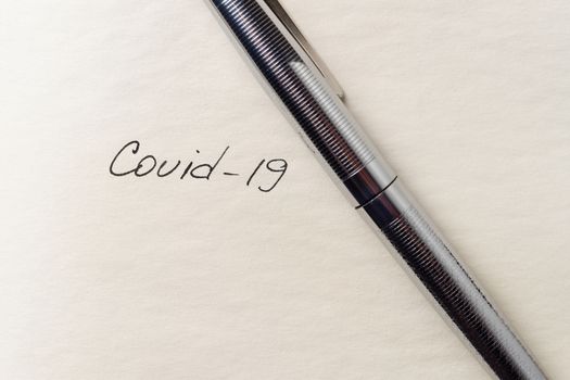 Covid-19 inscription on a blank empty sheet of paper in a notebook. Nearby lies a fountain pen. A lot of space for inscriptions and copyspace. The virus is dangerous. Blank for inscriptions. Template for article or cover.