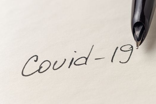 Covid-19 inscription on a blank empty sheet of paper in a notebook. Nearby lies a fountain pen. A lot of space for inscriptions and copyspace. The virus is dangerous. Blank for inscriptions. Template for article or cover.