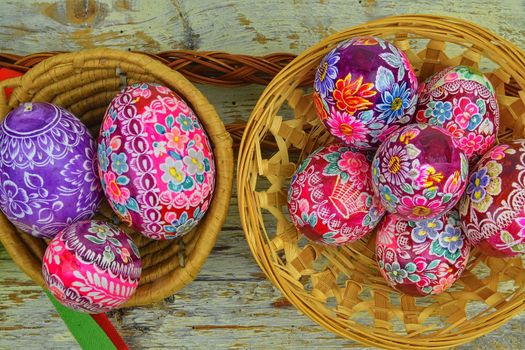 Still life with Easter eggs.  Decorated Easter eggs lay in a wicker basket on a white wooden background, top view. Easter eggs, decorated with traditional folk designs - east Europe, Czech Republic