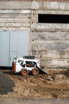 White skid steer loader at a construction site working with a soil. Industrial machinery. Industry