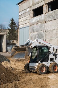 White skid steer loader at a construction site working with a soil. Industrial machinery. Industry