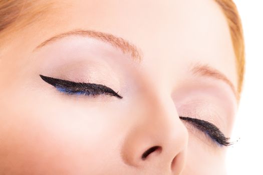 Close-up beauty shot of pretty young model with classic eyeliner, black and blue mascara, glowing clean skin and blond hair. Beauty and make up concept. Closeup macro shot of fashionable eyeliner on closed eyes.