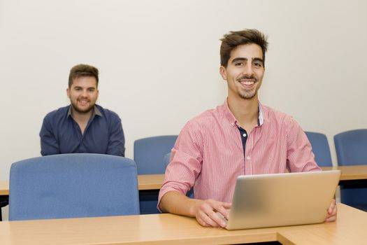 two young happy men at the classroom with a computer